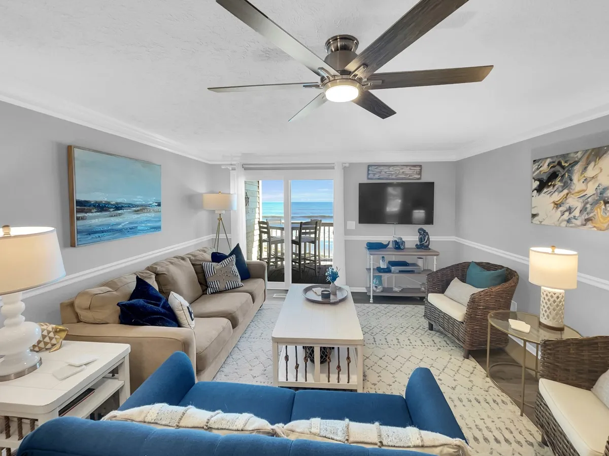 A tranquil living room scene featuring a blue sofa facing a large window with ocean views. There’s also a coffee table and tasteful artwork on the walls, encapsulating comfort and relaxation.