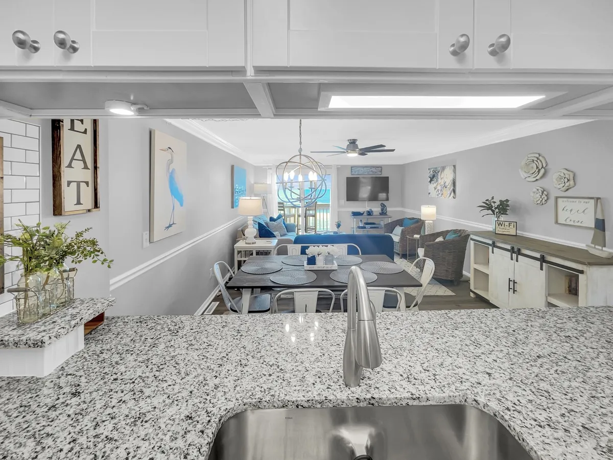 This angle captures the granite countertop and fully renovated kitchen, as well as the adjoining dining and living areas. Decorative wall art and comfortable seating enhance the sense of a connected, welcoming space for cooking, dining, and relaxing.