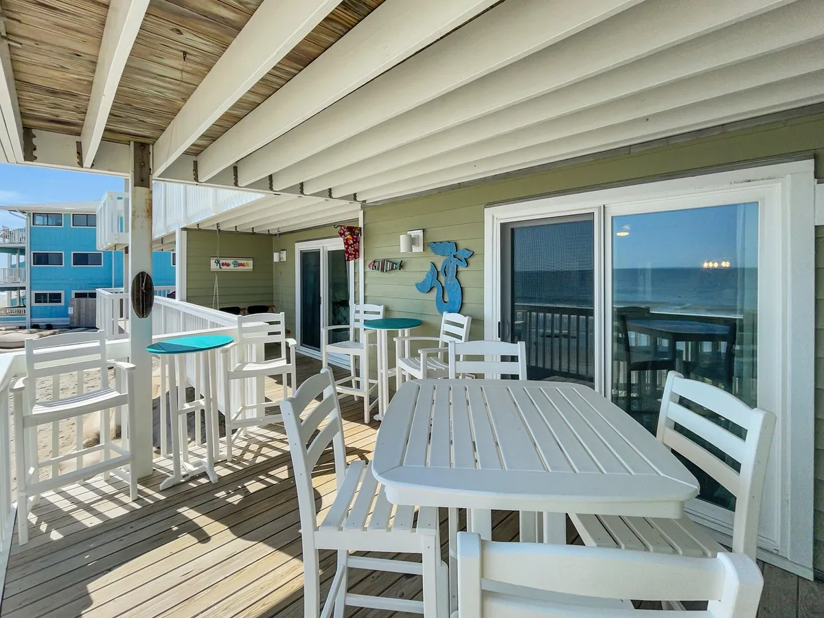 A spacious outdoor dining area with views of the ocean, decorated with blue fish decor. The table is set up for social gatherings or meals, and the scene shines with natural light and open air. The overall mood is casual, inviting, and perfect for enjoying time together as a group.