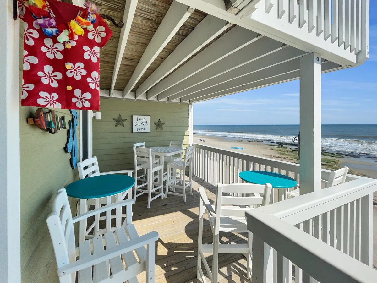 This exterior image shows a cheerful outdoor seating area with a decorative beach-themed wall art and a direct ocean view. Comfortable chairs are set up for enjoying coffee, reading, or relaxing while looking out over the water.