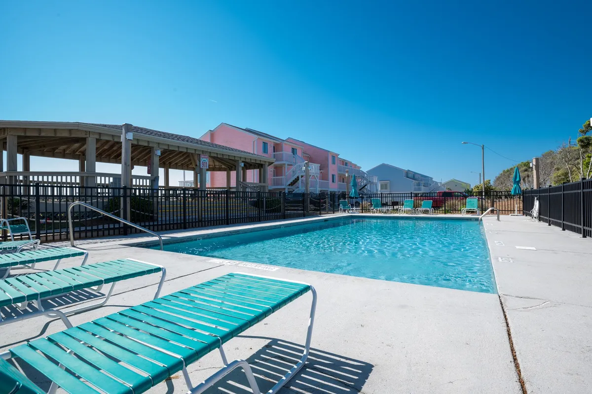 This exterior shot showcases a swimming pool surrounded by lounge chairs, with colorful buildings in the background. The mood is leisurely, ideal for family swimming, sunbathing, or gathering with loved ones around the pool.