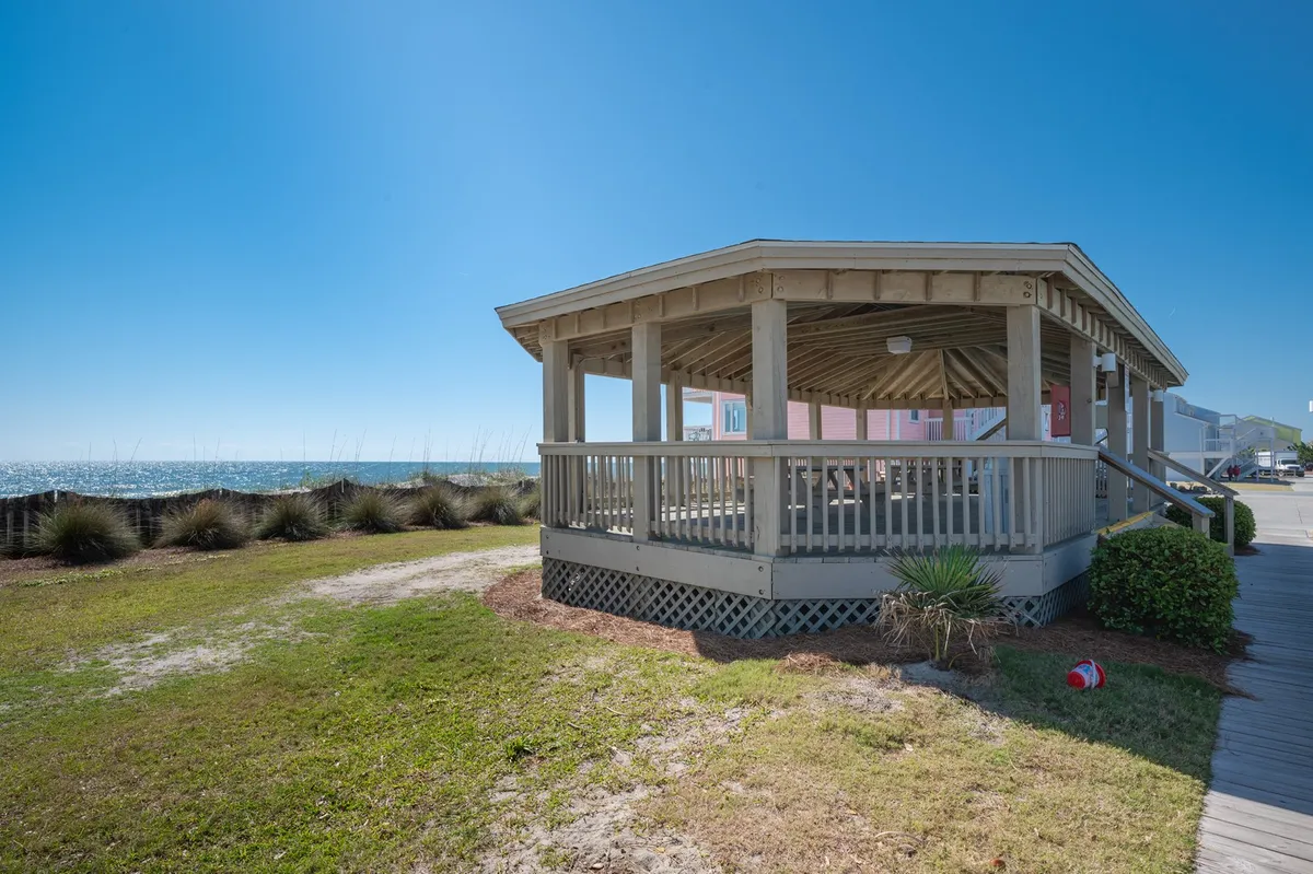 An inviting beach gazebo with an ocean view anchors this exterior image, accompanied by a landscaped grassy area. The scene is ideal for relaxing, gathering, or watching the sunset with loved ones, all set against a picturesque coastal backdrop.