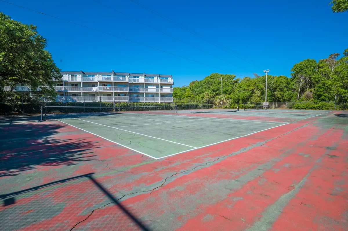An exterior view of a well-maintained tennis court surrounded by greenery, with an apartment building visible in the background. The court is ready for play, inviting guests to enjoy a friendly match or some active recreation.