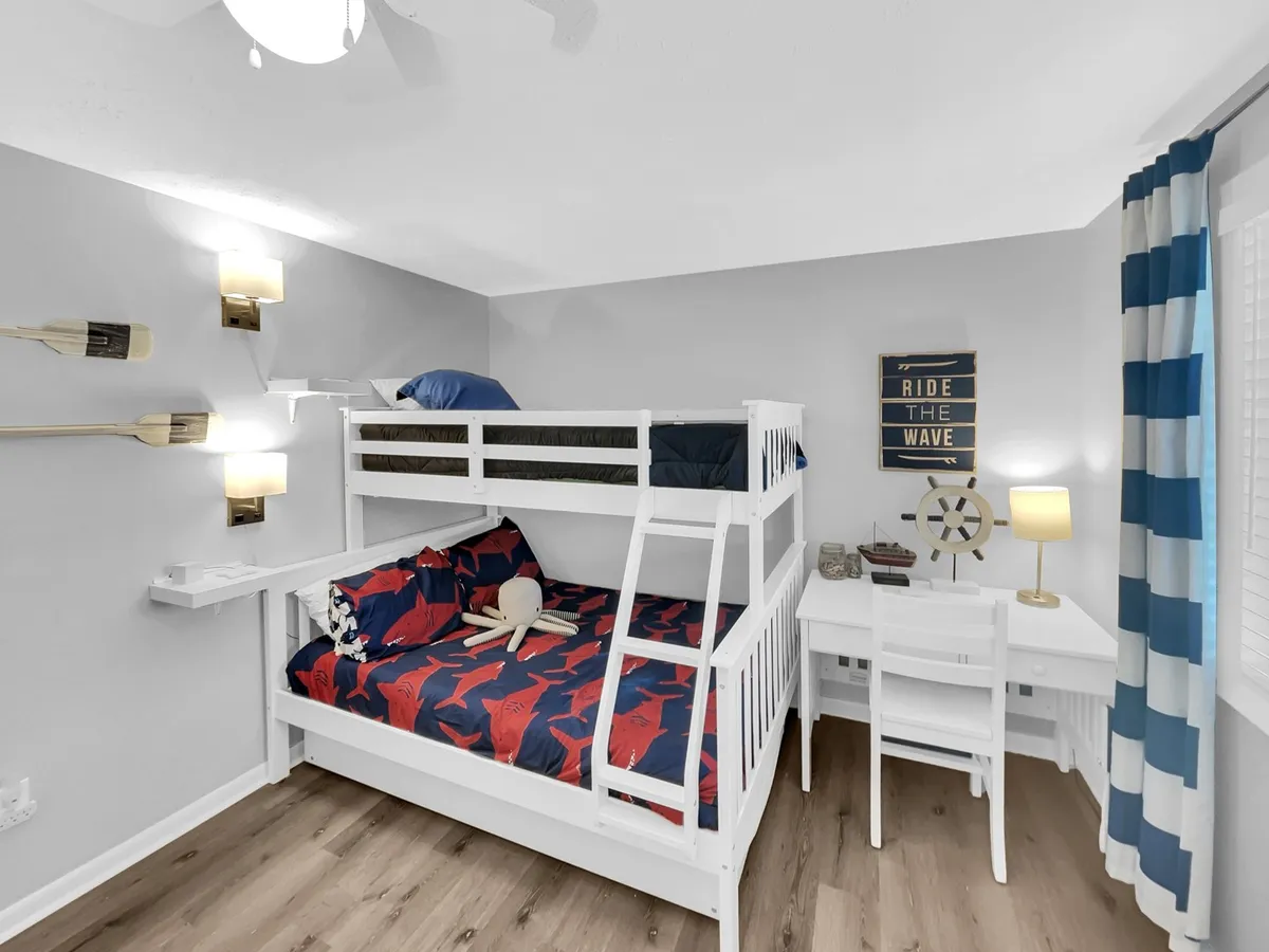 A cheerful and cozy bedroom set up with a twin-over-full bunk bed featuring nautical-themed bedding, a functional desk and chair for quiet activities, decorative wall art, and warm sconces, creating a playful yet practical environment.