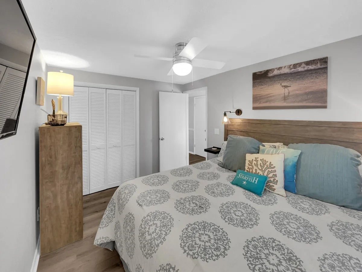 A cozy guest bedroom highlighted by a comfortable bed with decorative pillows, wall art above the headboard, and a nightstand with a lamp. The space is filled with soft, natural light, creating an inviting atmosphere.