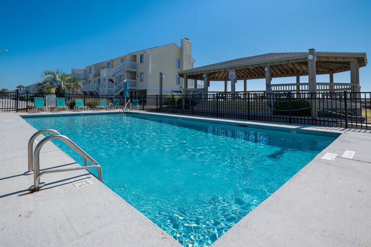 A sparkling swimming pool is surrounded by loungers and a gazebo, all set against a backdrop of blue skies and lush landscaping. The setup is inviting for sunbathing, socializing, or enjoying a refreshing dip.
